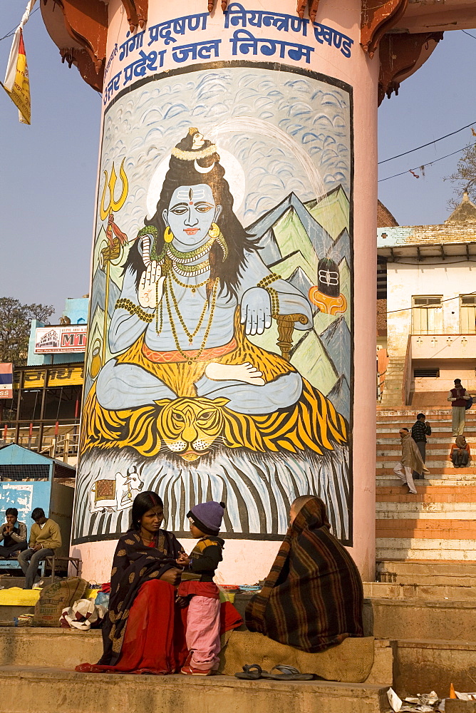 Indian people go about their daily business in front of a pillar painted with the Hindu god Shiva on that ghats of Varanasi, Uttar Pradesh, India, Asia