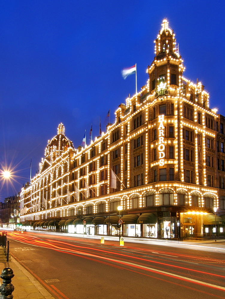 Exterior of the Harrods department store in the Knightsbridge area of London. Photographed at dusk using a long exposure to create traffic light trails in the street.