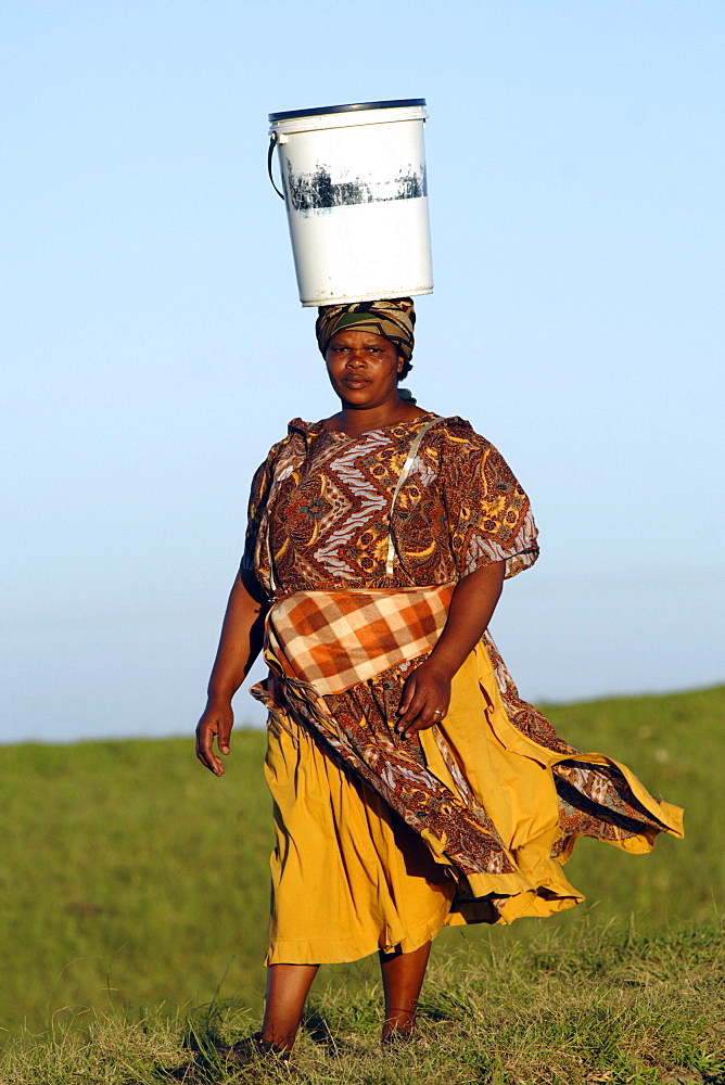 A Xhosa woman walking with a bucket of water on her head, as is traditional in the Eastern Cape Province of South Africa.