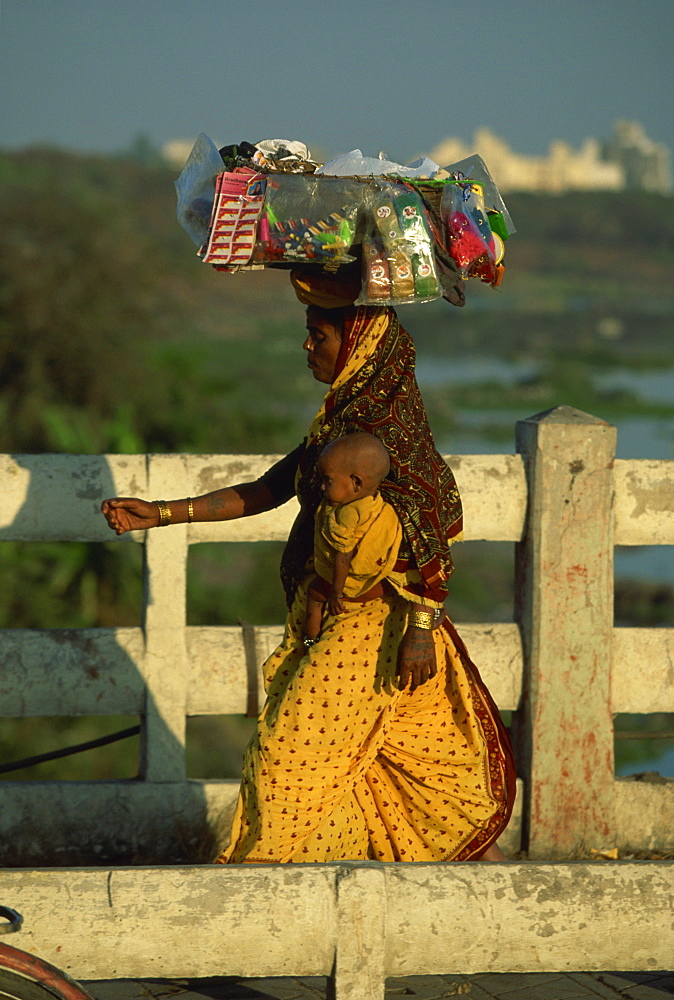 Street vendor carrying her wares and baby crossing the Mula River, Pune, Maharashtra state, India, Asia