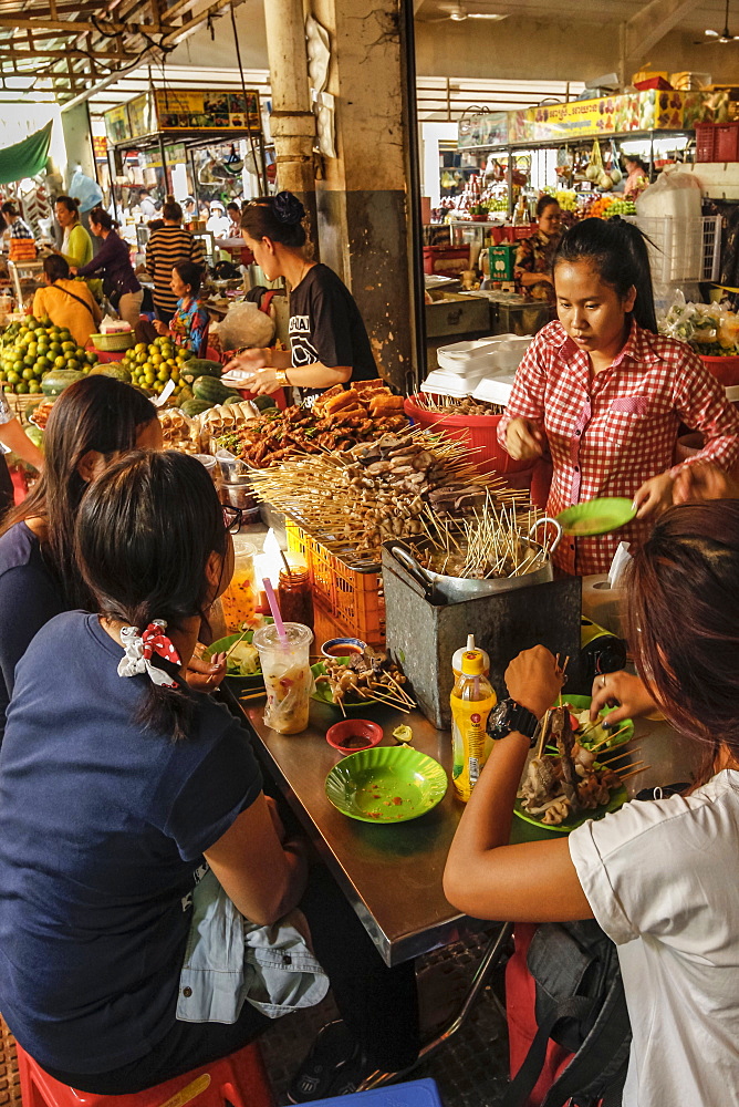 Young women eating sate at a stall in the eating area of this huge old market, Central Market, city centre, Phnom Penh, Cambodia, Indochina, Southeast Asia, Asia