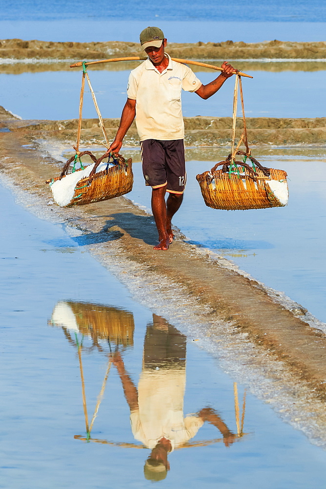 Man with shoulder pole harvesting the salt fields around the Praek Tuek Chhu River estuary south of the city, Kampot, Cambodia, Indochina, Southeast Asia, Asia