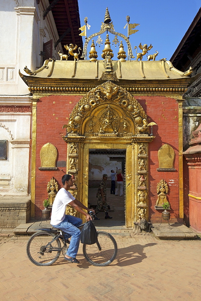 Man cycling past the Golden Gate, Sun Dhoka, in Durbar Square, Bhaktapur, UNESCO World Heritage Site, Kathmandu Valley, Nepal, Asia