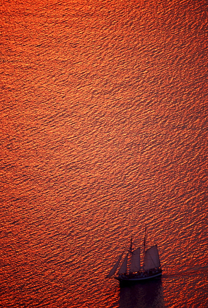 Sailing ship in the gleaming red Mediterranean Sea off the island of Santorini, Cyclades, Greece, Europe