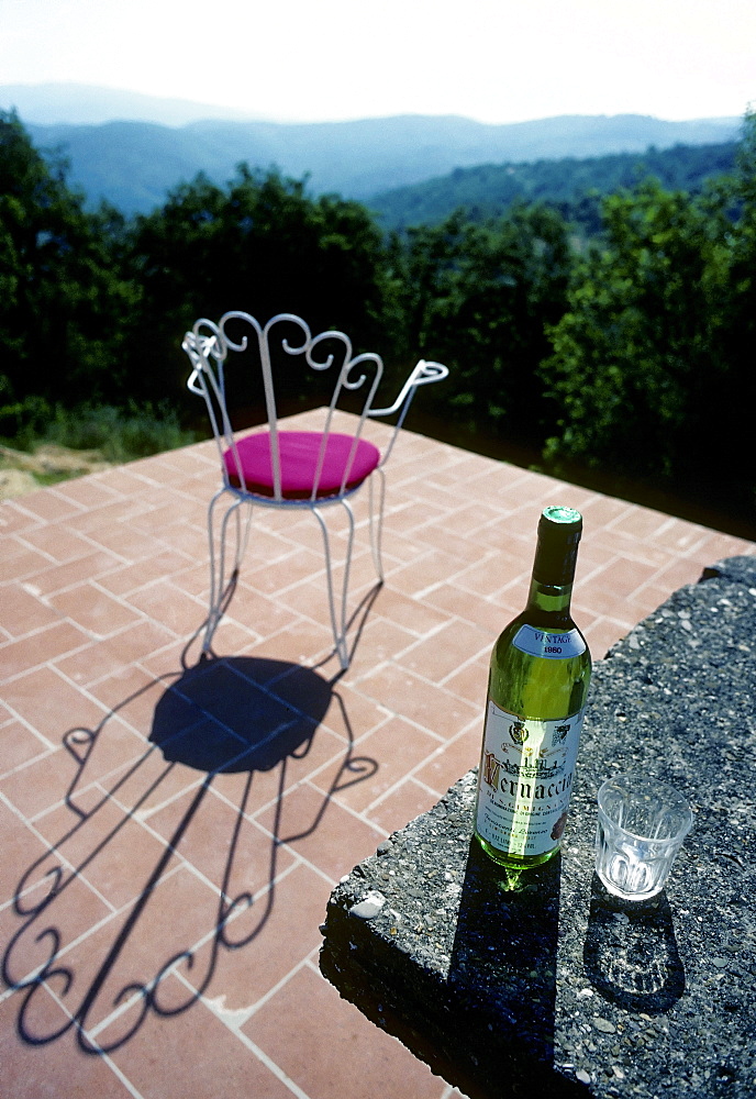 Solitary chair on a terrace overlooking the Chianti region, fantastic views, bottle of white wine and a glass on a table, holiday atmosphere, Sienna, Tuscany, Italy, Europe