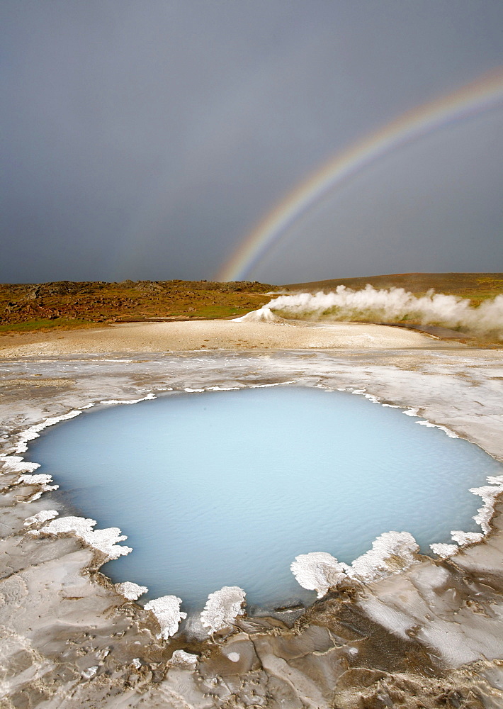 Blahver, blue spring, the most beautiful blue water pool in Hveravellir in the Highlands, in front of Oeskjuholt, a steaming calc-sinter mound which looks like a mini volcano, below a rainbow, Hveravellir, Iceland, Europe