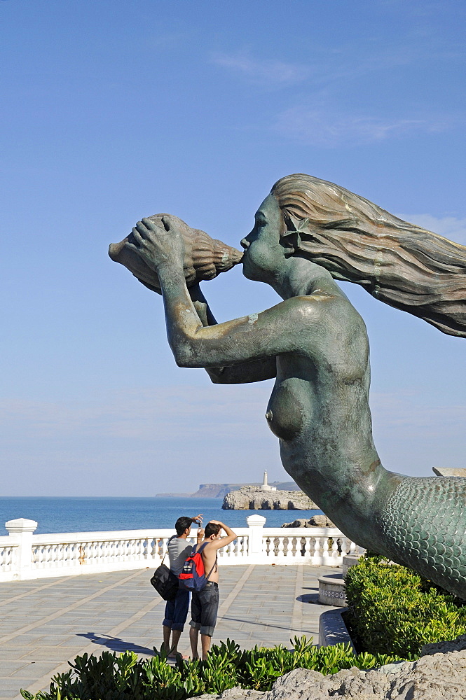 Tourists standing next to the sculpture of a mermaid blowing a chonch shell, La Magdalena peninsula, Santander, Cantabria, Spain, Europe