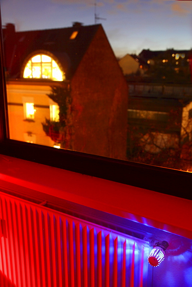 Radiator at a window with an illuminated thermostat, heating costs