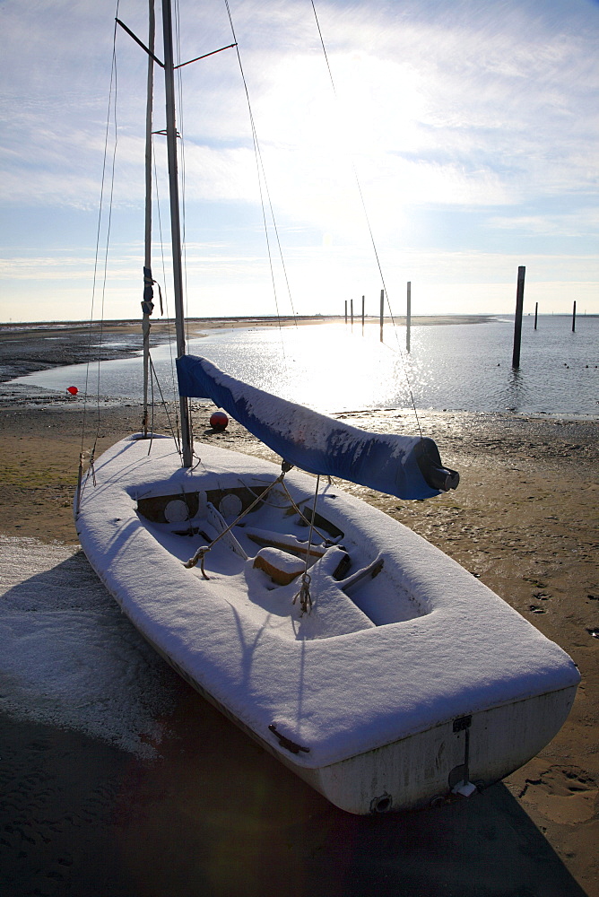 Bay in the Wadden Sea with a sailing boat, snow-covered beach on the East Frisian North Sea island of Spiekeroog, Lower Saxony, Germany, Europe