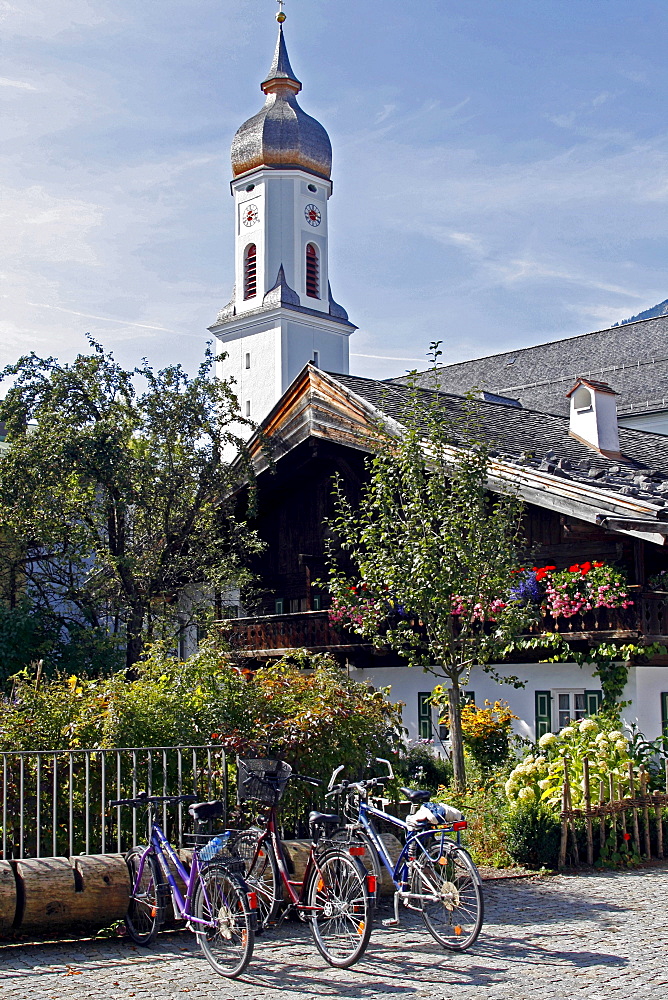 Traditional Bavarian buildings with balconies and flowers, a church behind, Garmisch-Partenkirchen, Bavaria, Germany, Europe