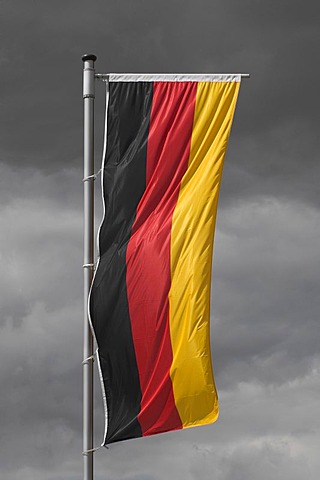 Germany flag hanging vertically in front of a gray cloudy sky