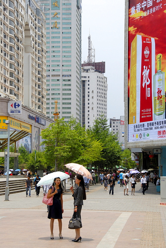 Two women with an umbrella, busy pedestrian zone in the modern city center, Kunming, Yunnan Province, People's Republic of China, Asia