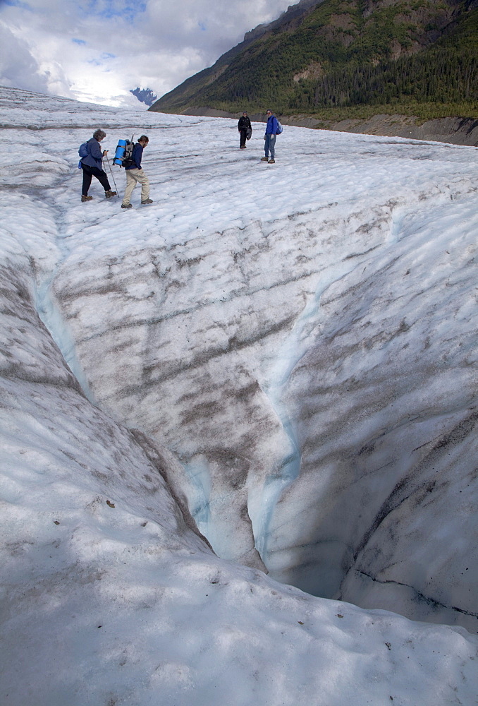 Hikers on the Root Glacier in Wrangell-St. Elias National Park pass a moulin, where meltwater descends into the glacier, Kennicott, Alaska, USA