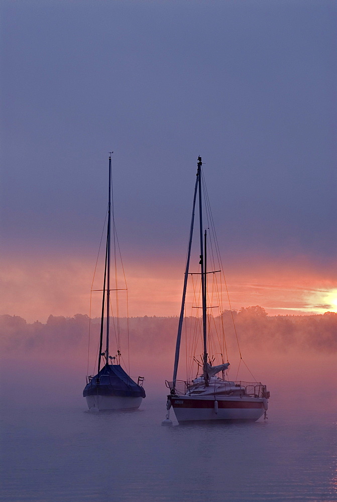 Sun rising behind sailing boats and fog over Ammersee lake, Bavaria, Germany, Europe