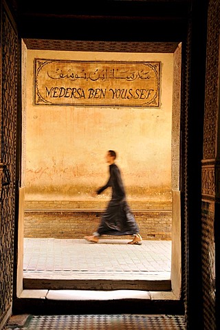 Man wearing a cloak walking through an alley at the Ben Youssef Madrasah, Qur'an school, in the medina quarter of Marrakesh, Morocco, Africa