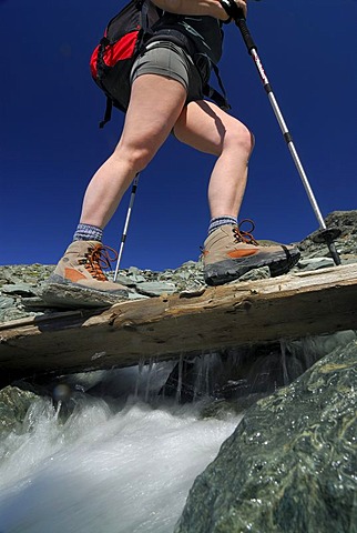 Hiker crossing a wooden bridge above a mountain brook, National Park Hohe Tauern, Tyrol, Austria