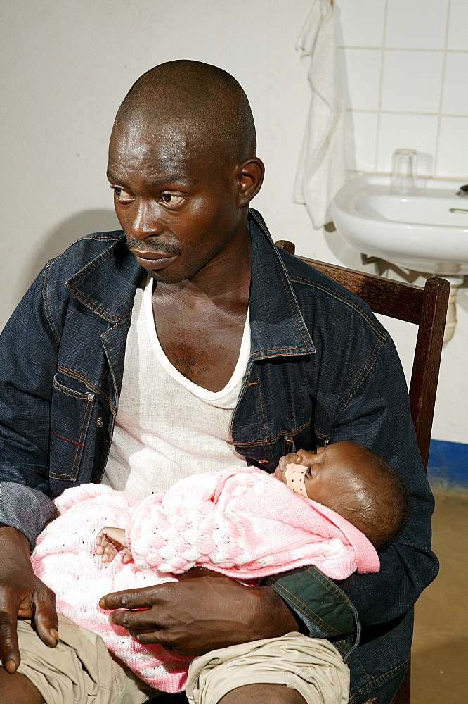 Father holding his HIV-infected infant on his lap, Cameroon, Africa