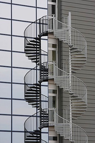 Spiral staircase in front of a facade of glass and stone