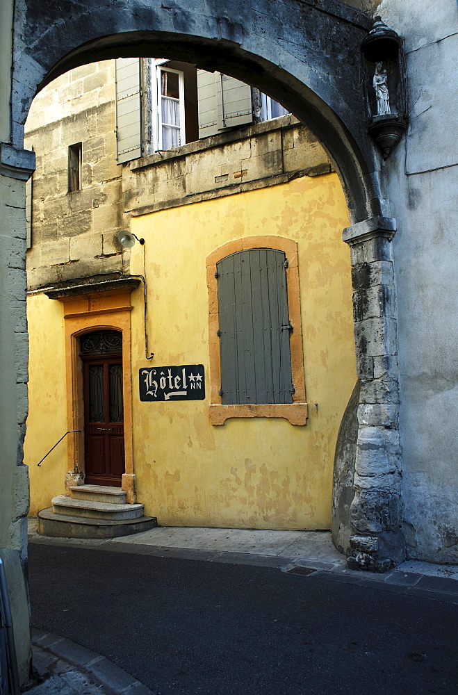 Entrance with sign to abandoned two star hotel viewed from beneath an old stone arch in a narrow street in Arles, France