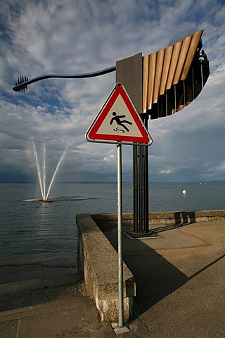 Sign warns of slipping danger, water fountain in the background and modern windrose in Rorschach am Bodensee, St. Gallen, Switzerland