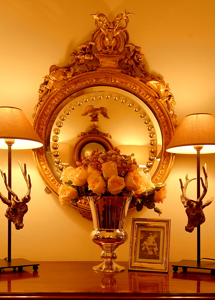 Artificial flowers in a vase placed in front of a gold-framed mirror