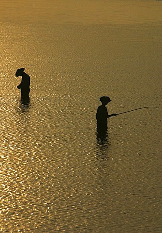 Silhouettes of fishermen standing in the water at sunset