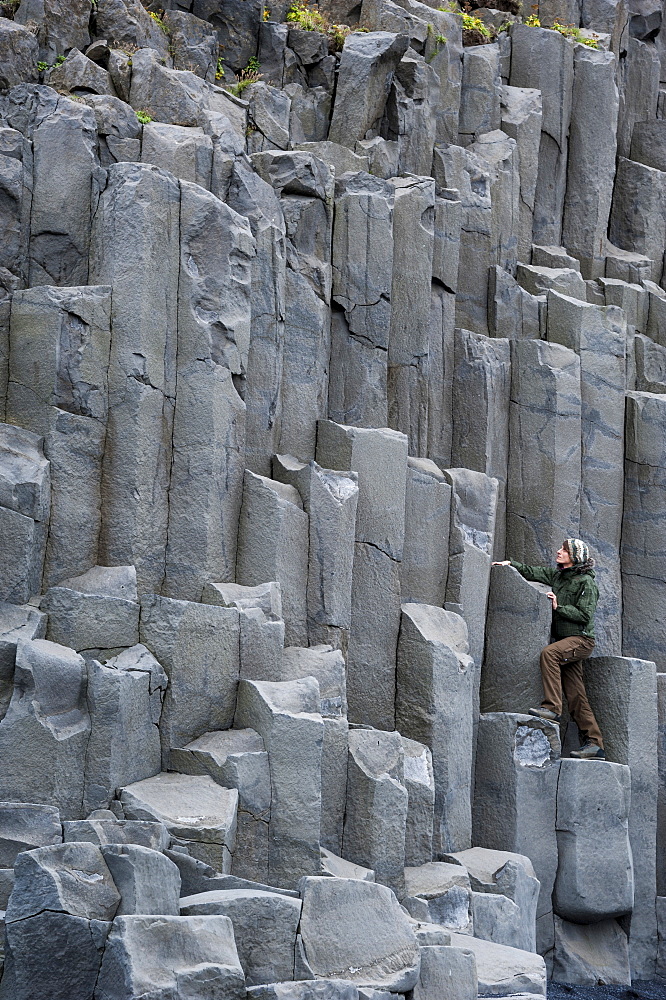 Woman climbing on basalt columns, Halsanefshellir cave, Reynisfjara beach at Vik i Myrdal, South Coast, Iceland, Europe