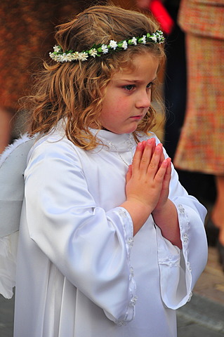 Little blond girl dressed as an angel in white with wings, flower garland and hands clasped in prayer during the Semana Santa, Holy Week festivities in La Nucia, Costa Blanca, Spain