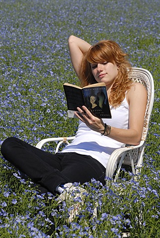 Reading girl sitting in a chair in a field of linen