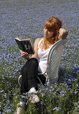 Reading girl sitting in a chair in a field of linen