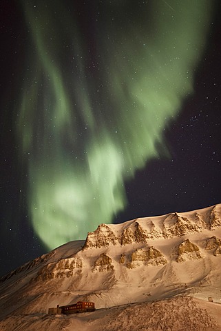 Strong green Northern Lights, Aurora Borealis, above a historic building lit by the lights of the town of Longyearbyen, Longyearbreen Glacier at back, Spitsbergen, Svalbard, Norway, Europe