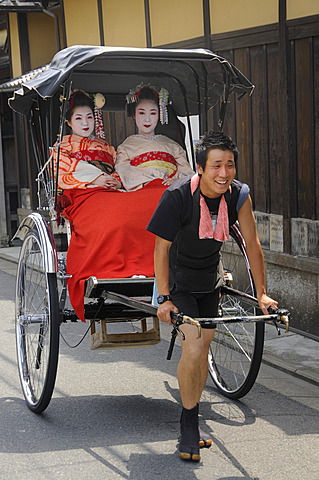 Maikos, apprentice Geishas, being pulled by a rickshaw driver through the historic city centre of Kyoto, Japan, Asia