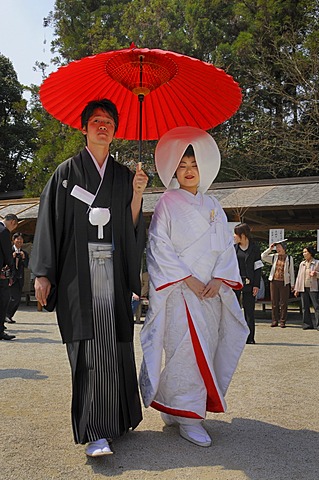 Japanese wedding couple wearing traditional wedding kimonos, bride wearing a bonnet, groom holding a red parasol in front of the Kamigamo Shrine, Kyoto, Japan, Asia