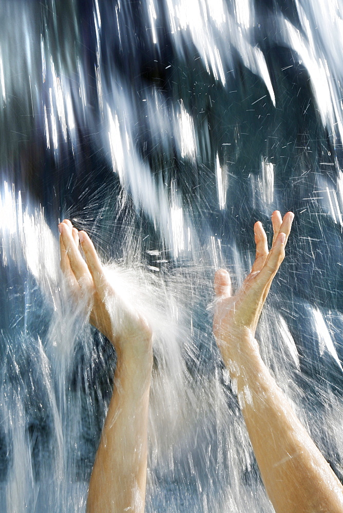 Water of a waterfall flowing and splashing over two hands