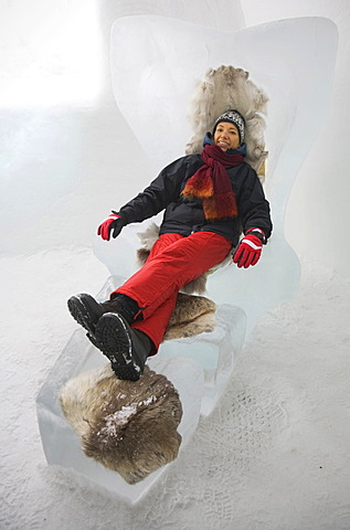 Tourist on an armchair made of ice, sitting on reindeer fur against the cold, Jukkasjaervi, Lappland, Northern Sweden