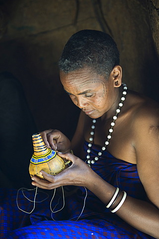 A woman of the Datoga tribe decorating a calabash with glass beads, Lake Eyasi, Tanzania, Africa