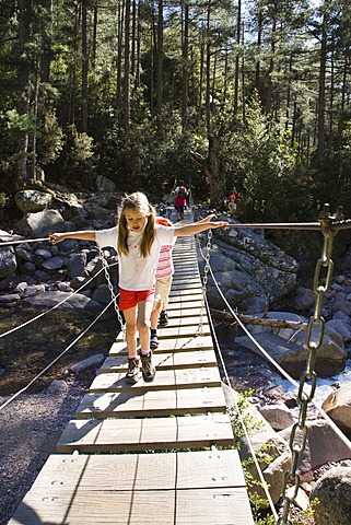 7-year-old girls on suspension bridge over Spasmiata river, Foret de Bonifatu, Corsica, France, Europe