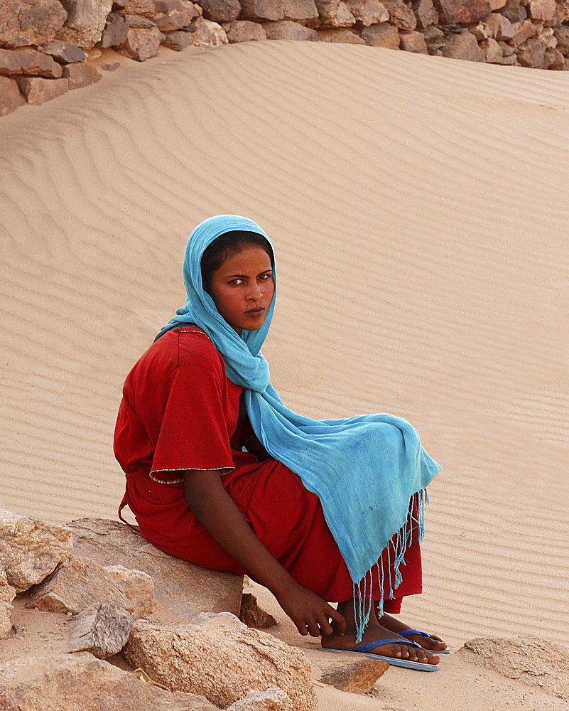 Young woman in colourful clothes sitting on stone, oasis of Al-Ghazali, Sudan, Africa