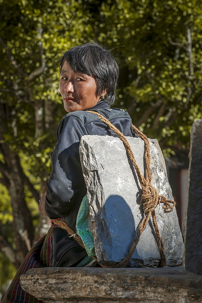 A woman taking a rest, with building materials, a stone slab on her back, Himalayas, Kingdom of Bhutan