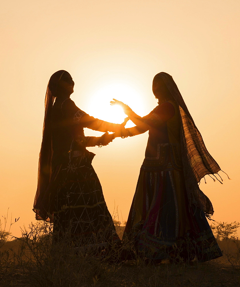 Two women in dresses dancing in front of the setting sun, Pushkar Camel Fair, Pushkar, Rajasthan, India, Asia