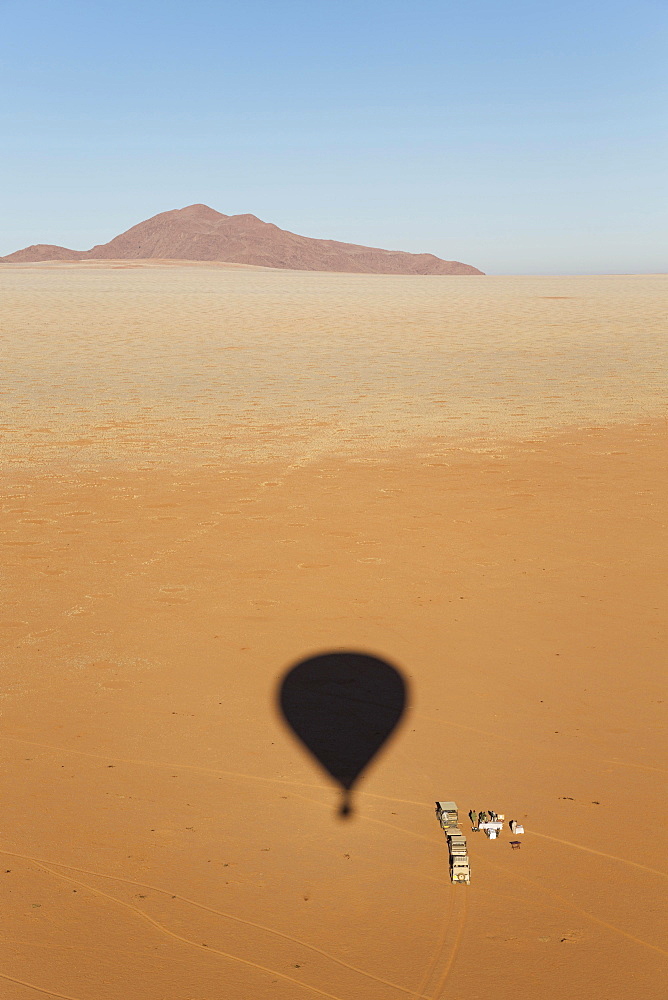 Shadow of a hot-air balloon at the intended landing spot in a true desert environment, ground crew prepares an opulent breakfast, photographed from the basket of the balloon, Namib Desert, NamibRand Nature Reserve, Namibia, Africa