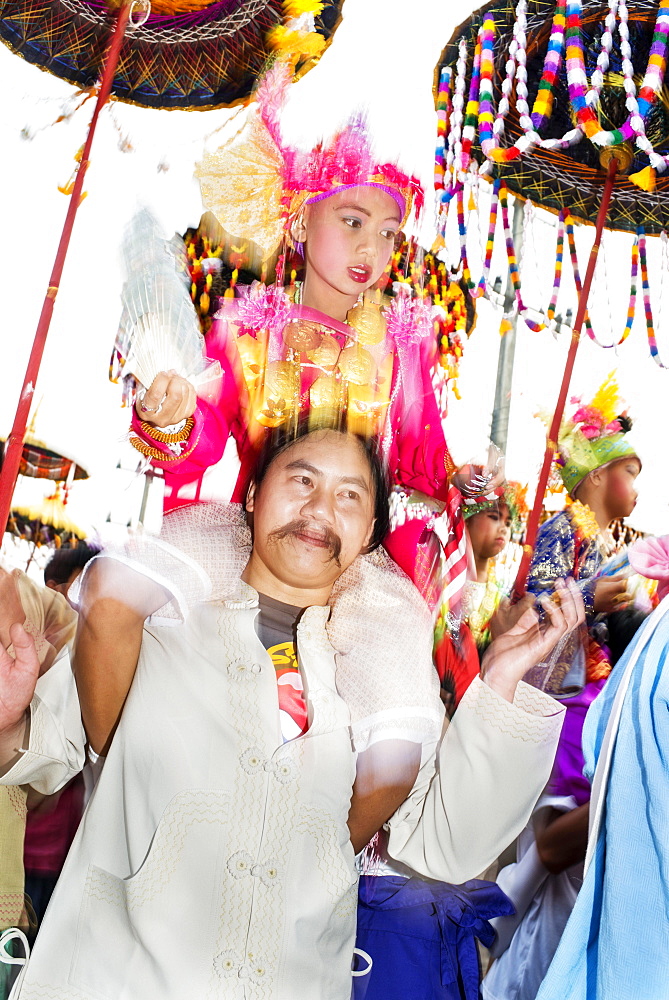 Boy holding a fan, dressed in a bright coloured costume, on the shoulders of male family member, at the annual Poi Sang Long festival, Mae Hong Son, Thailand, Asia