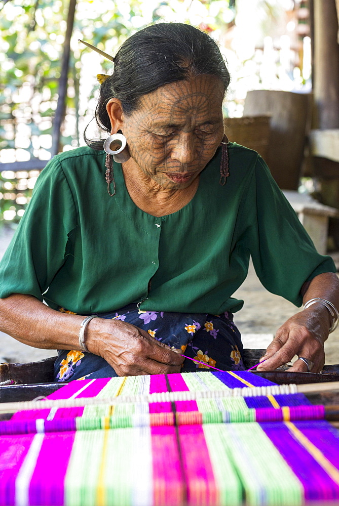 Woman with traditional facial tattoos and ear jewellery from the Chin people, ethnic group, the last of their kind, weaving on a loom, Rakhine State, Myanmar, Asia