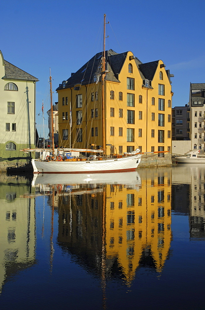 Yellow house and a sailing boat reflected in the calm water of the inner harbor of Alesund, Alesund, Moere og Romsdal, Norway, Europe