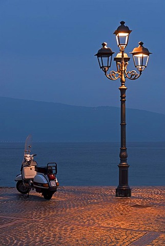 A Motorino scooter beside a street lamp at the shore of Lake Garda at the blue hour in Gargnano, Lombardia, Italy, Europe