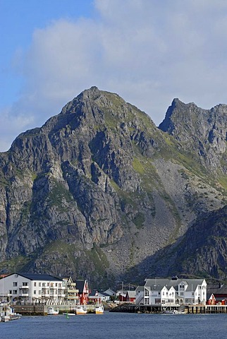 The steep rocks of the Lofoten archipelago behind the fishing boats and typical red and white houses in HenningsvÃŠr, Nordland, Norway, Europe