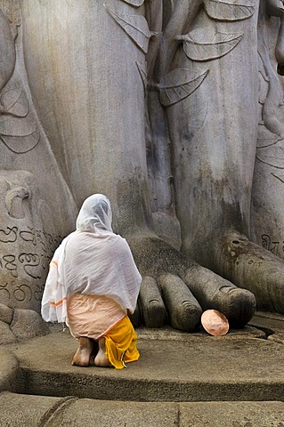 A Jain pilgrim is praying at the feet of the statue of Lord Gomateshwara, the tallest monolithic statue in the world, dedicated to Lord Bahubali, carved out of a single block of granite stone, 18 meters high, 983 AD, Sravanabelagola, Karnataka, India, Asi