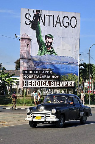 Vintage car driving in front of revolutionary propaganda poster, "Santiago siempre heroica", Spanish for "Santiago is always heroic", Plaza de la Revolucion, Santiago de Cuba, Cuba, Caribbean