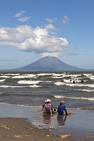 People sitting on the shallow shore of Lago de Nicaragua with the volcanic island of Ometepe and the stratovolcano Volcan Concepcion at back, San Jorge, Nicaragua, Central America