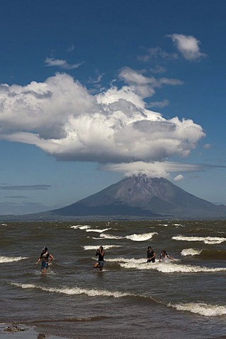 People walking on the shallow shore of Lago de Nicaragua, volcanic island of Ometepe and the stratovolcano Volcan Concepion at back, San Jorge, Nicaragua, Central America